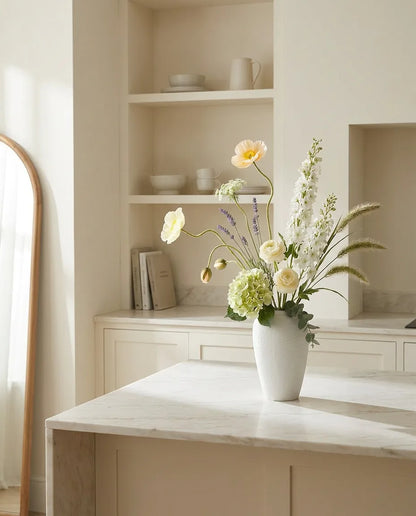 Bouquet artificiel blanc et vert sur un îlot en marbre clair dans une cuisine crème