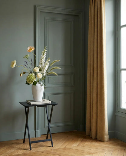 Bouquet artificiel blanc et vert dans une entrée à la porte vert sauge, sur une table d'appoint noire