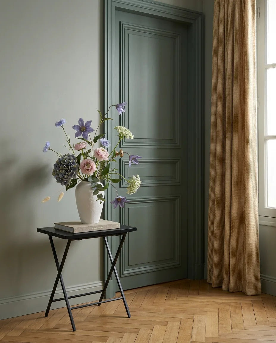 Bouquet artificiel bleu et rose dans une entrée à la porte vert sauge, sur une table d'appoint noire