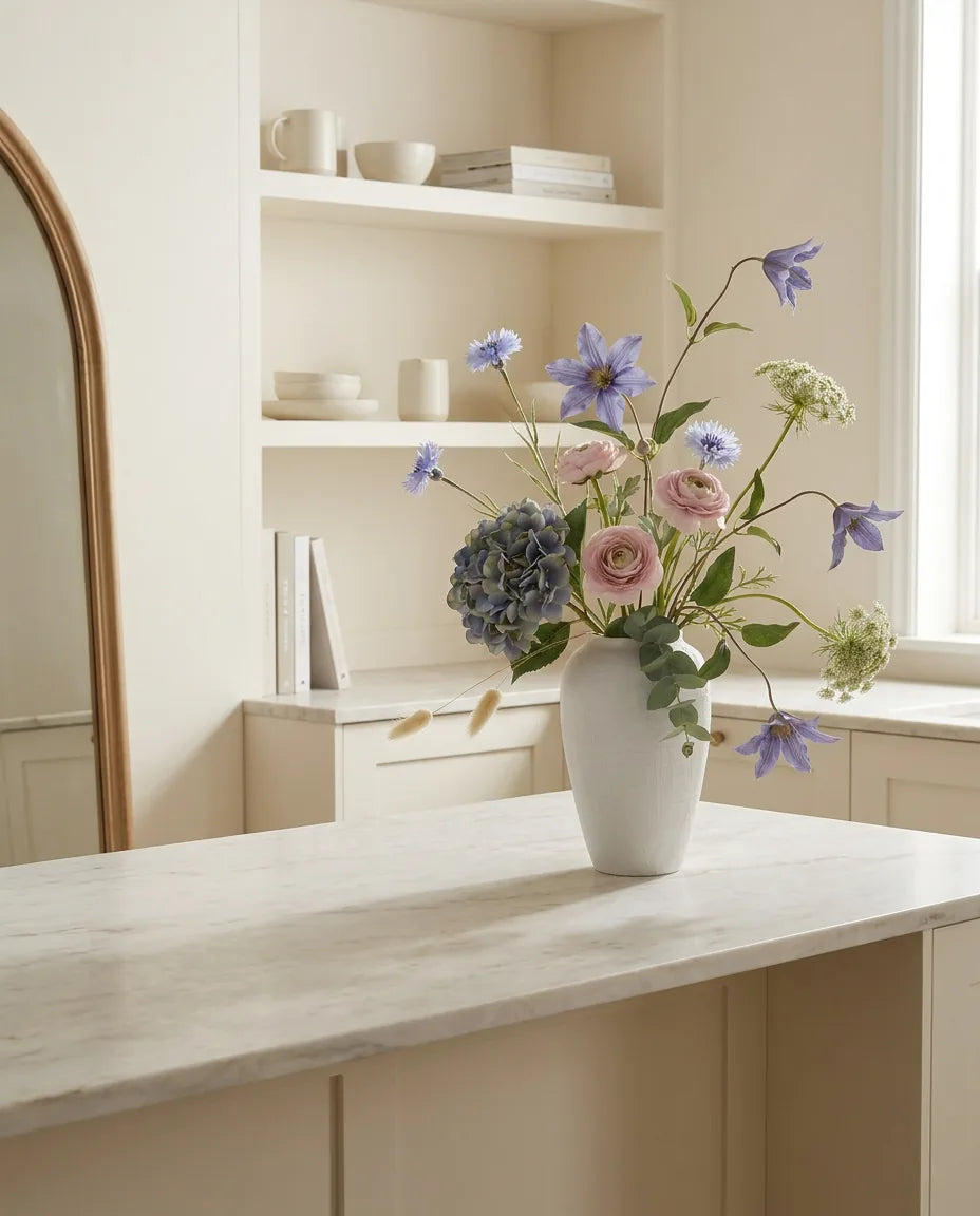 Bouquet artificiel bleu et rose sur un îlot en marbre clair dans une cuisine crème