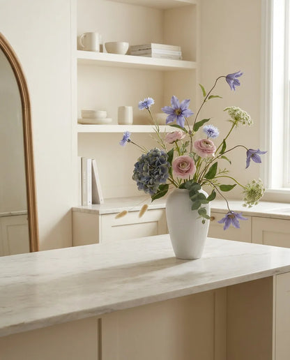 Bouquet artificiel bleu et rose sur un îlot en marbre clair dans une cuisine crème