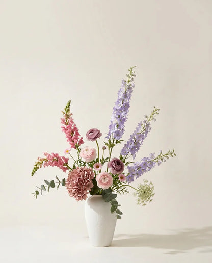 Bouquet artificiel d'hortensias, delphiniums et renoncules violet et rose dans un vase en céramique