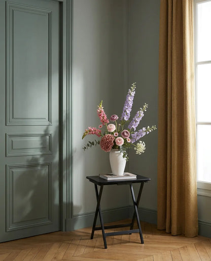 Bouquet artificiel violet et rose dans une entrée à la porte vert sauge, sur une table d'appoint noire