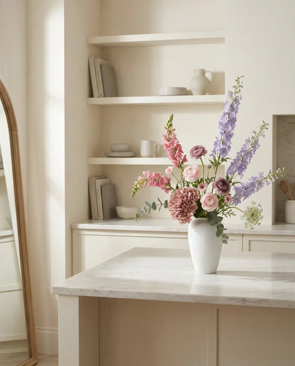 Bouquet artificiel violet et rose sur un îlot en marbre clair dans une cuisine crème