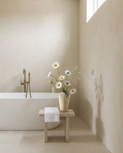 Bouquet artificiel blanc et jaune près d'une baignoire îlot, sur un tabouret en pierre, robinetterie laiton