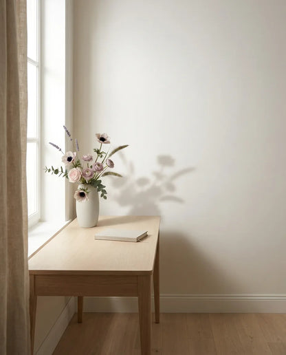 Bouquet artificiel rose et violet sur un bureau en chêne clair près d'un rideau en lin