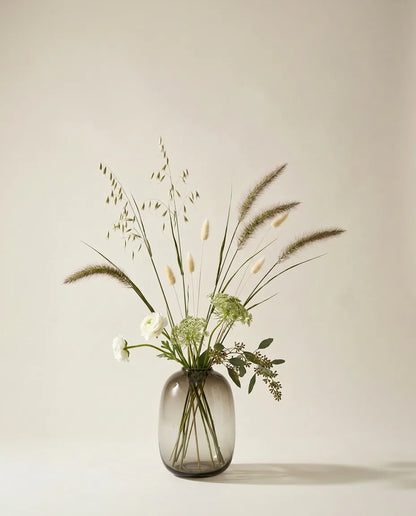 Bouquet artificiel de renoncules, pennisetum et lagurus vert et blanc dans un vase en verre ambré