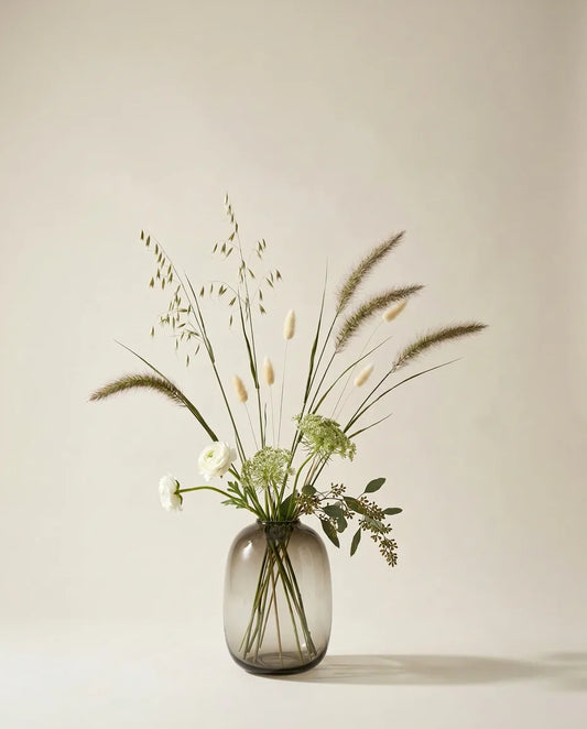 Bouquet artificiel de renoncules, pennisetum et lagurus vert et blanc dans un vase en verre ambré