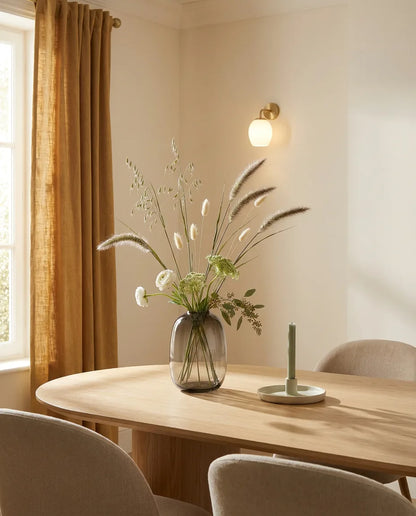 Bouquet artificiel vert et blanc sur une table ovale en chêne clair dans une salle à manger, applique laiton