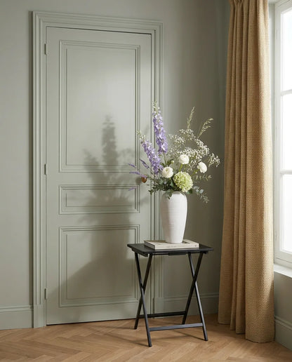Bouquet artificiel violet et blanc dans une entrée à la porte vert sauge, sur une table d'appoint noire