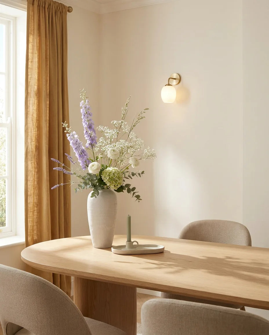 Bouquet artificiel violet et blanc sur une table ovale en chêne clair dans une salle à manger, applique laiton