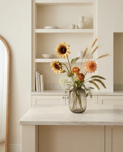 Bouquet artificiel orange et beige sur un îlot en marbre clair dans une cuisine crème