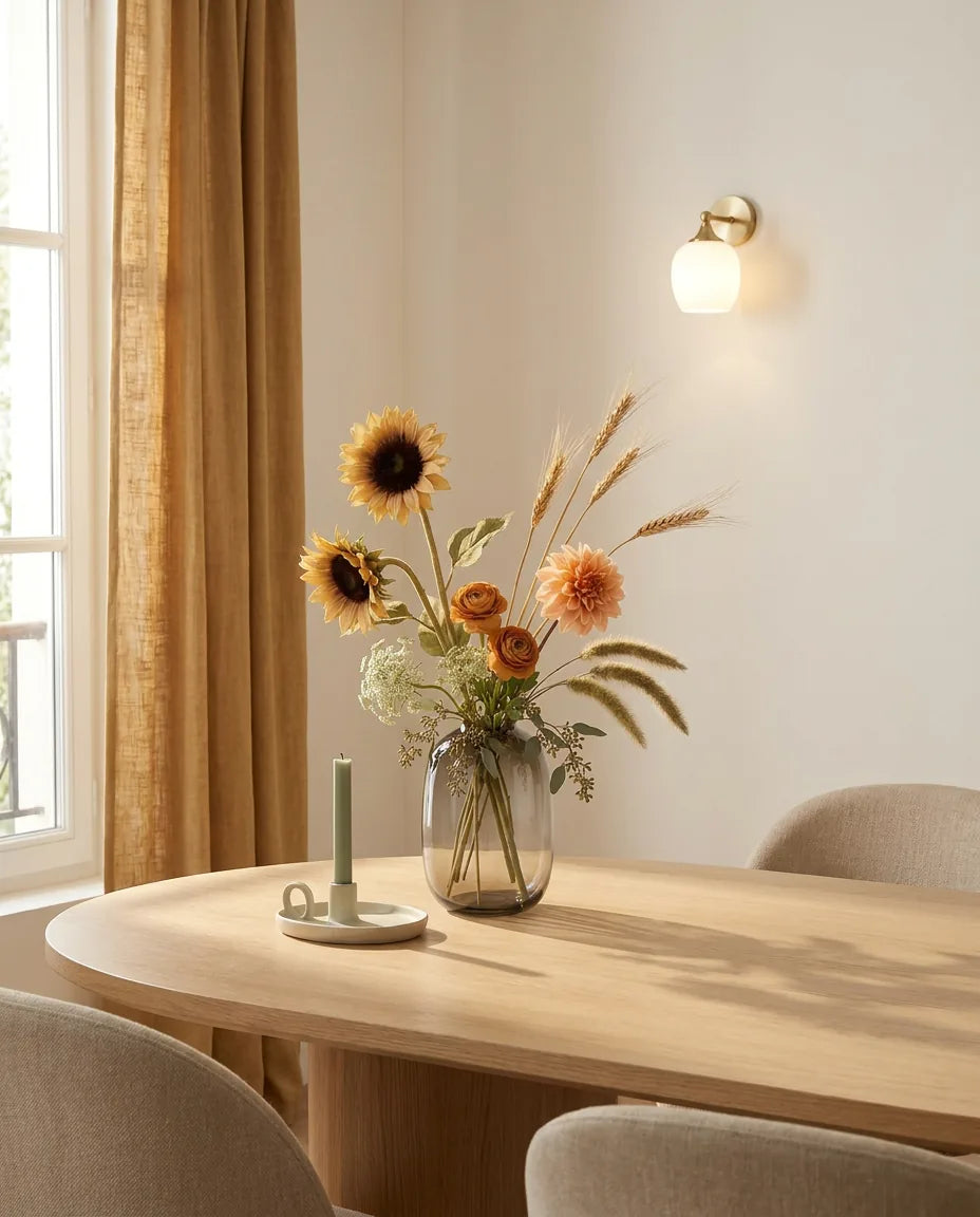 Bouquet artificiel orange et beige sur une table ovale en chêne clair dans une salle à manger, applique laiton