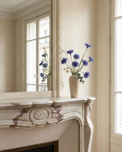 Bouquet artificiel blanc et bleu sur une cheminée en marbre devant un grand miroir, salon parisien
