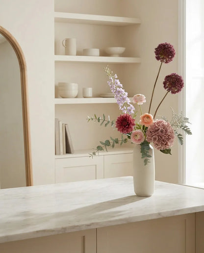 Bouquet artificiel rose et violet sur un îlot en marbre clair dans une cuisine crème
