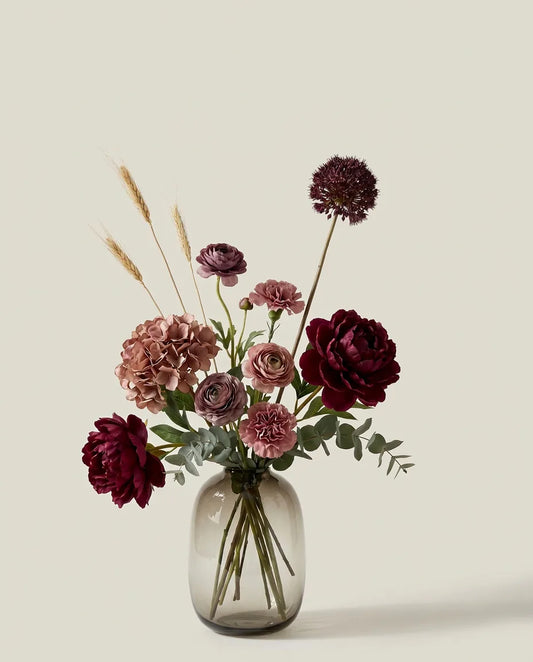 Bouquet artificiel de pivoines, hortensias et renoncules rouge et violet dans un vase en verre ambré
