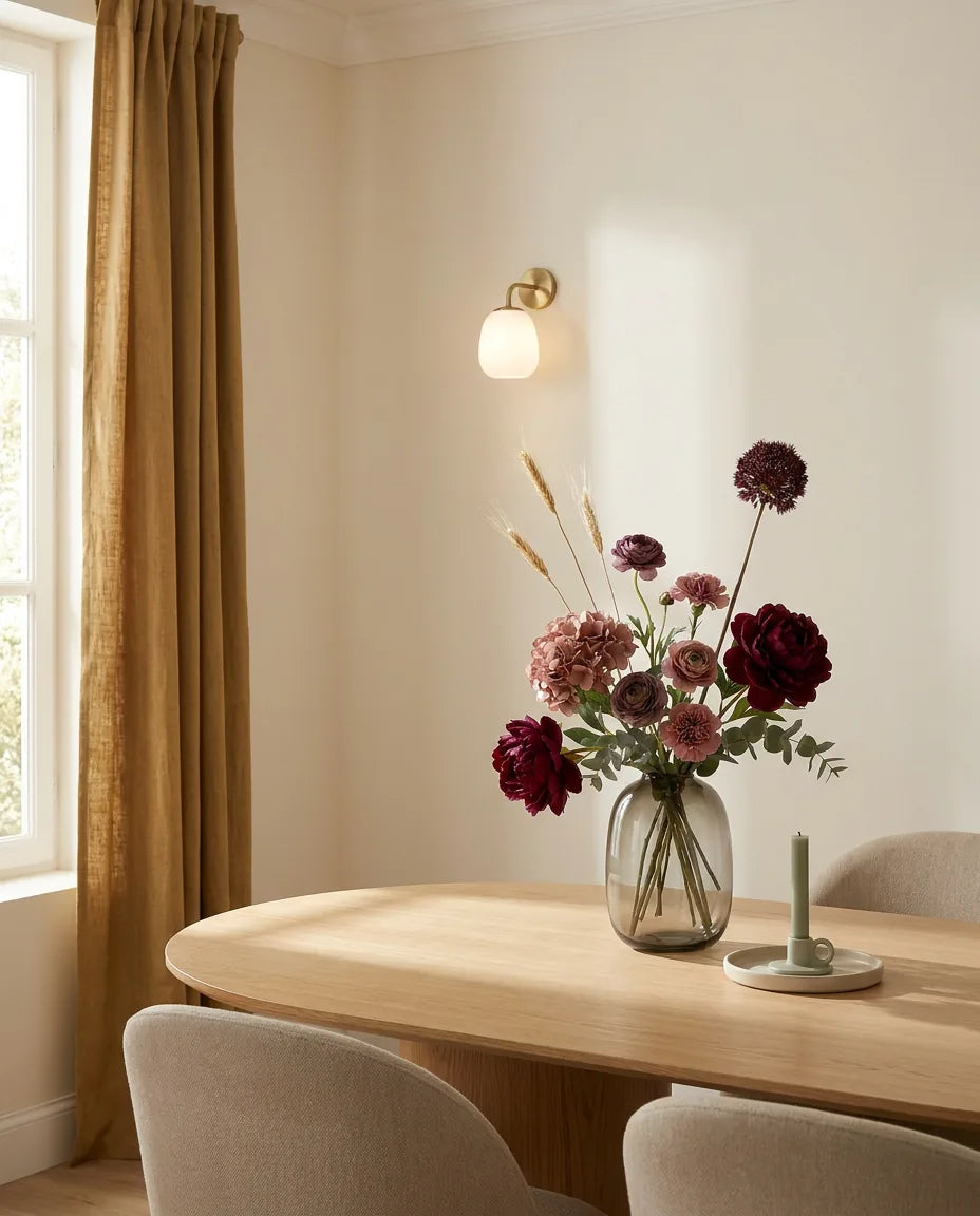 Bouquet artificiel rouge et violet sur une table ovale en chêne clair dans une salle à manger, applique laiton