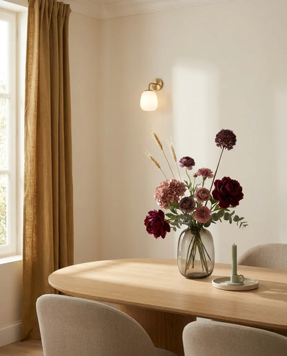 Bouquet artificiel rouge et violet sur une table ovale en chêne clair dans une salle à manger, applique laiton