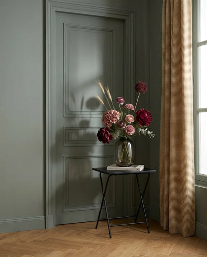 Bouquet artificiel rouge et violet dans une entrée à la porte vert sauge, sur une table d'appoint noire