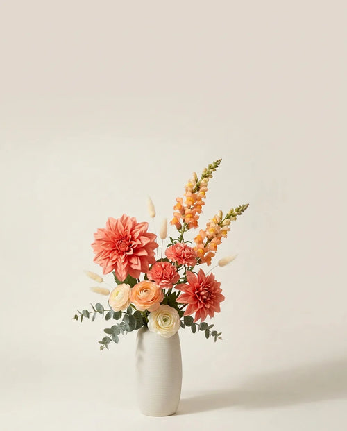 Bouquet artificiel de dahlias, renoncules et œillets orange et rose dans un vase en céramique