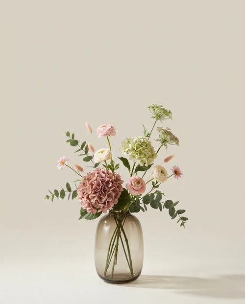 Bouquet artificiel d'hortensias, renoncules et marguerites rose et vert dans un vase en verre ambré