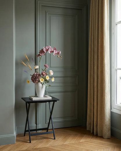 Bouquet artificiel violet et jaune dans une entrée à la porte vert sauge, sur une table d'appoint noire