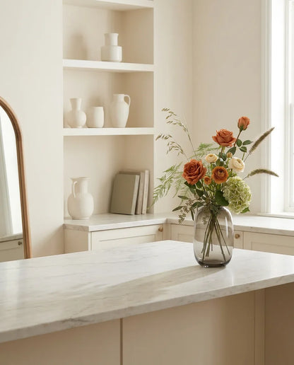 Bouquet artificiel orange et vert sur un îlot en marbre clair dans une cuisine crème