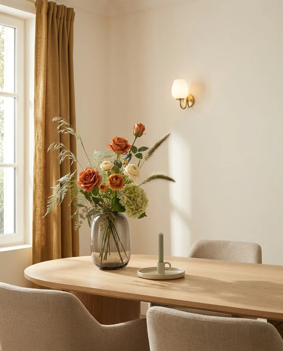 Bouquet artificiel orange et vert sur une table ovale en chêne clair dans une salle à manger, applique laiton