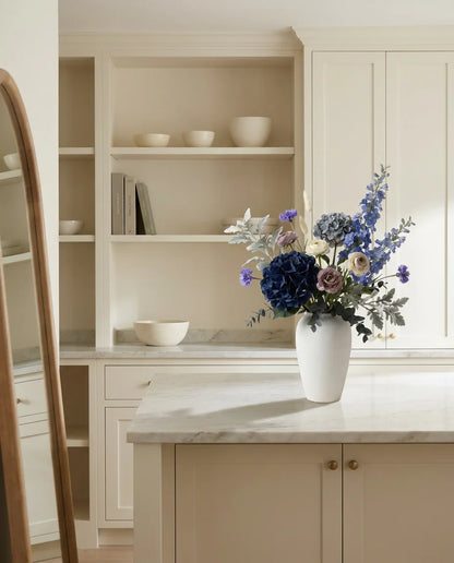 Bouquet artificiel bleu et violet sur un îlot en marbre clair dans une cuisine crème