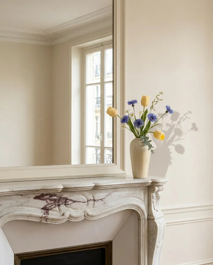 Bouquet artificiel jaune et bleu sur une cheminée en marbre devant un grand miroir, salon parisien