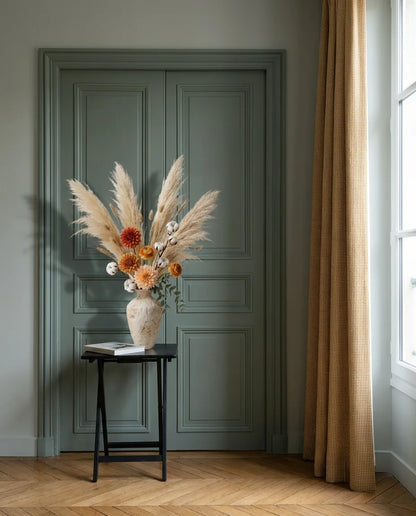 Bouquet artificiel beige et orange dans une entrée à la porte vert sauge, sur une table d'appoint noire