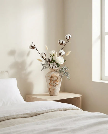 Bouquet artificiel blanc et beige sur une table de chevet en bois clair, près d'un linge en lin