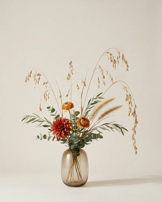 Bouquet artificiel de dahlias, renoncules et blé orange et beige dans un vase en verre ambré