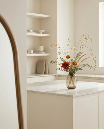Bouquet artificiel orange et beige sur un îlot en marbre clair dans une cuisine crème