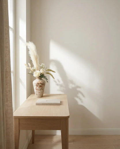 Bouquet artificiel blanc et beige sur un bureau en chêne clair, près d'un rideau en lin