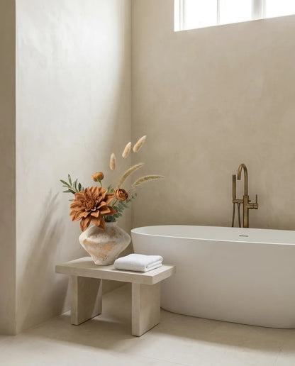 Bouquet artificiel orange et beige sur un tabouret en pierre près d'une baignoire îlot