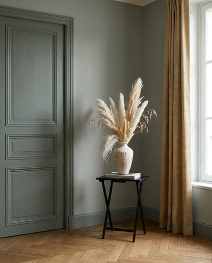 Bouquet artificiel beige et rose sur une table d'appoint noire près d'une porte vert sauge