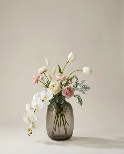 Bouquet artificiel d'orchidées, renoncules et tulipes blanc et rose dans un vase en verre ambré