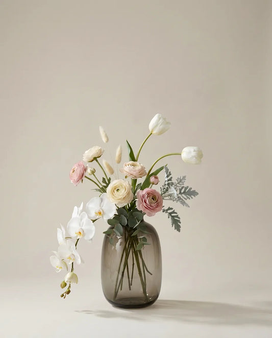 Bouquet artificiel d'orchidées, renoncules et tulipes blanc et rose dans un vase en verre ambré