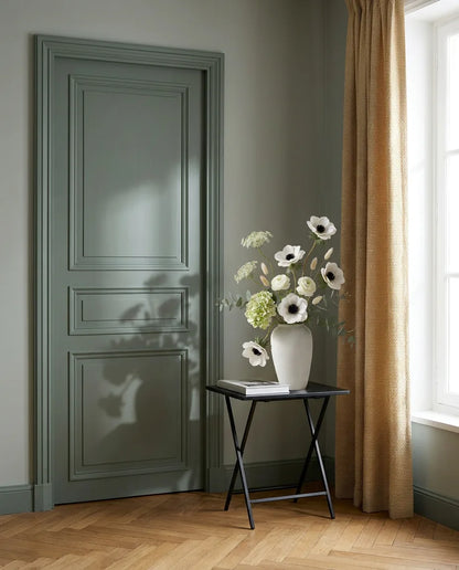 Bouquet artificiel blanc et vert sur une table d'appoint noire près d'une porte vert sauge