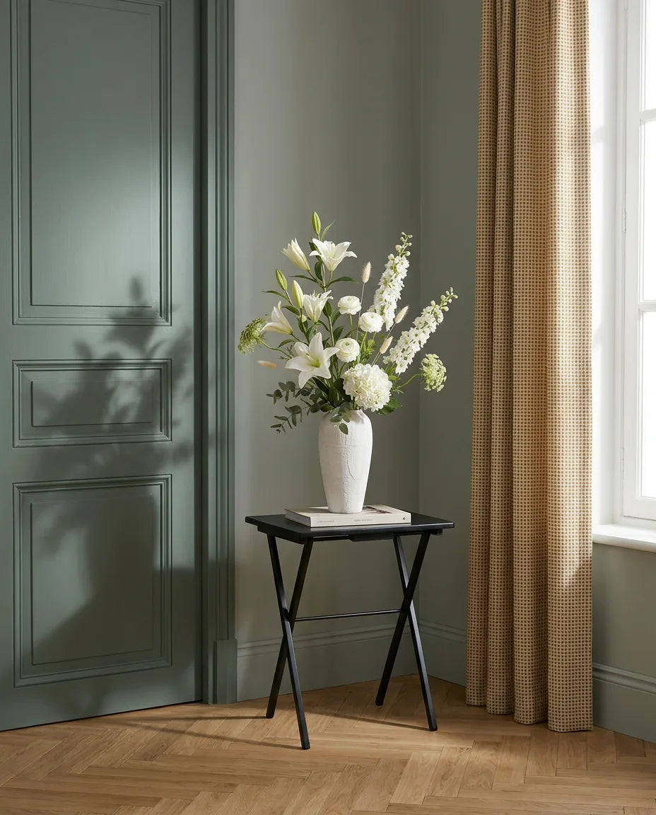 Bouquet artificiel blanc et vert sur une table d'appoint noire près d'une porte vert sauge
