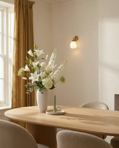Bouquet artificiel blanc et vert sur une table ovale en chêne clair dans une salle à manger