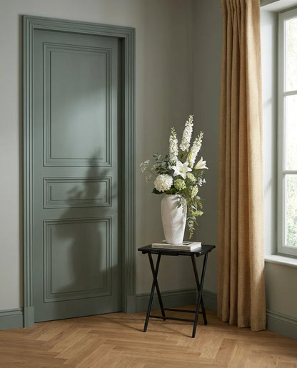 Bouquet artificiel blanc et vert sur une table d'appoint noire près d'une porte vert sauge