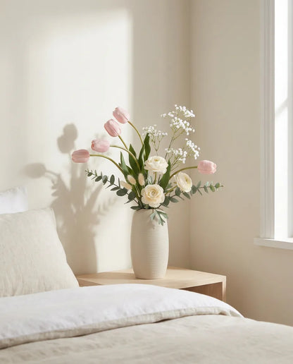 Bouquet artificiel rose et blanc sur une table de chevet en bois clair, près d'un linge en lin