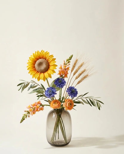 Bouquet artificiel de tournesols, scabiosa et mufliers jaune et bleu dans un vase en verre ambré