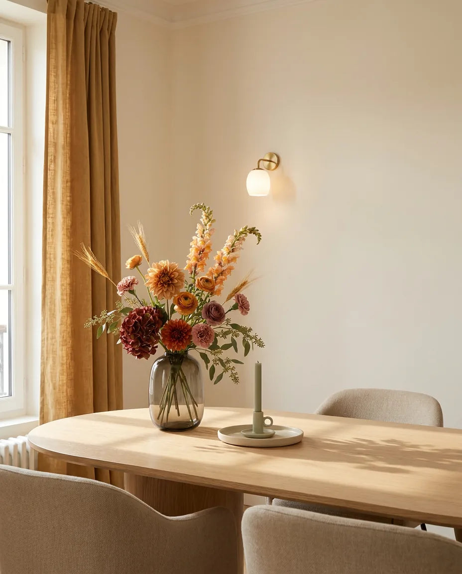 Bouquet artificiel orange et beige sur une table ovale en chêne clair dans une salle à manger