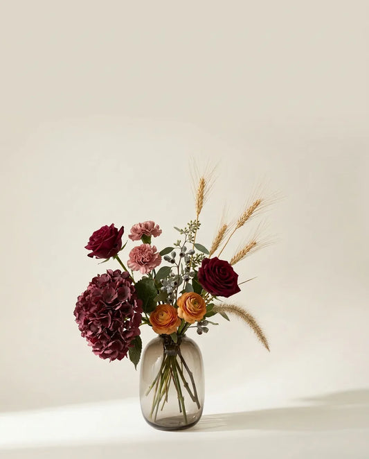 Bouquet artificiel de roses, hortensias et œillets rouge et rose dans un vase en verre ambré