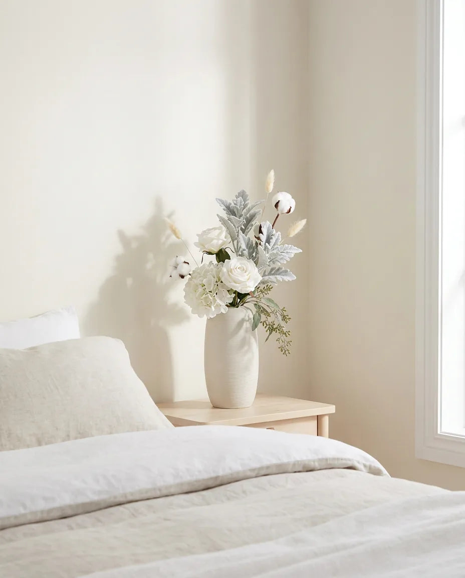 Bouquet artificiel blanc et vert sur une table de chevet en bois clair, près d'un linge en lin