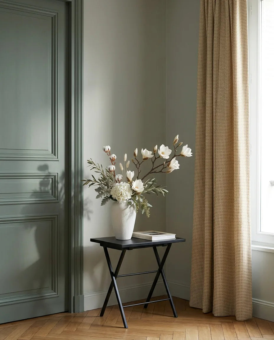 Bouquet artificiel blanc et beige sur une table d'appoint noire près d'une porte vert sauge