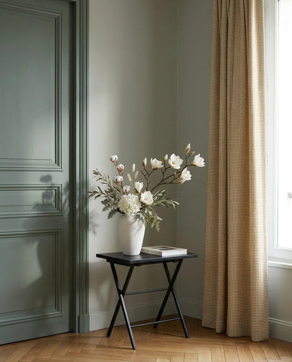 Bouquet artificiel blanc et beige sur une table d'appoint noire près d'une porte vert sauge